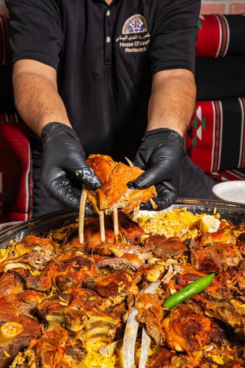 Chef hand-pulling slow-roasted lamb over saffron rice